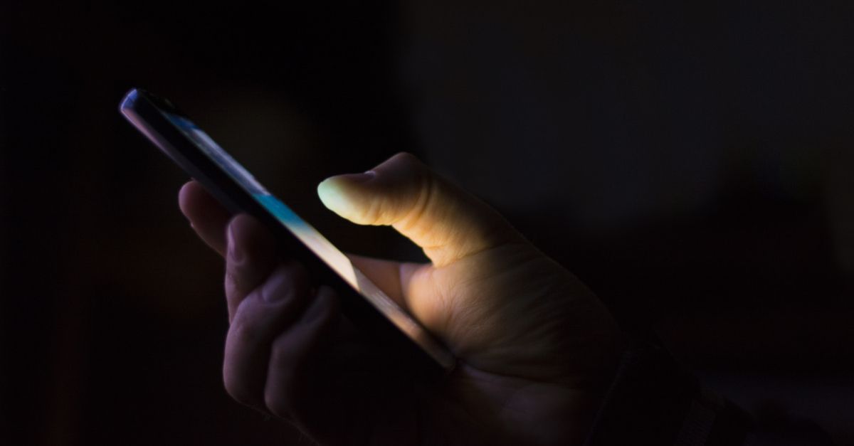 Hand holding mobile phone against dark background