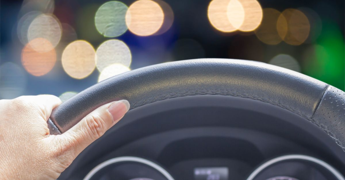 Woman's hand holding a steering wheel with bokeh lights in the background