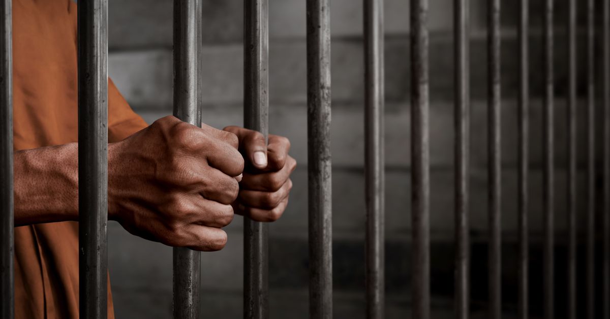 Hands gripping the bars of a jail cell.