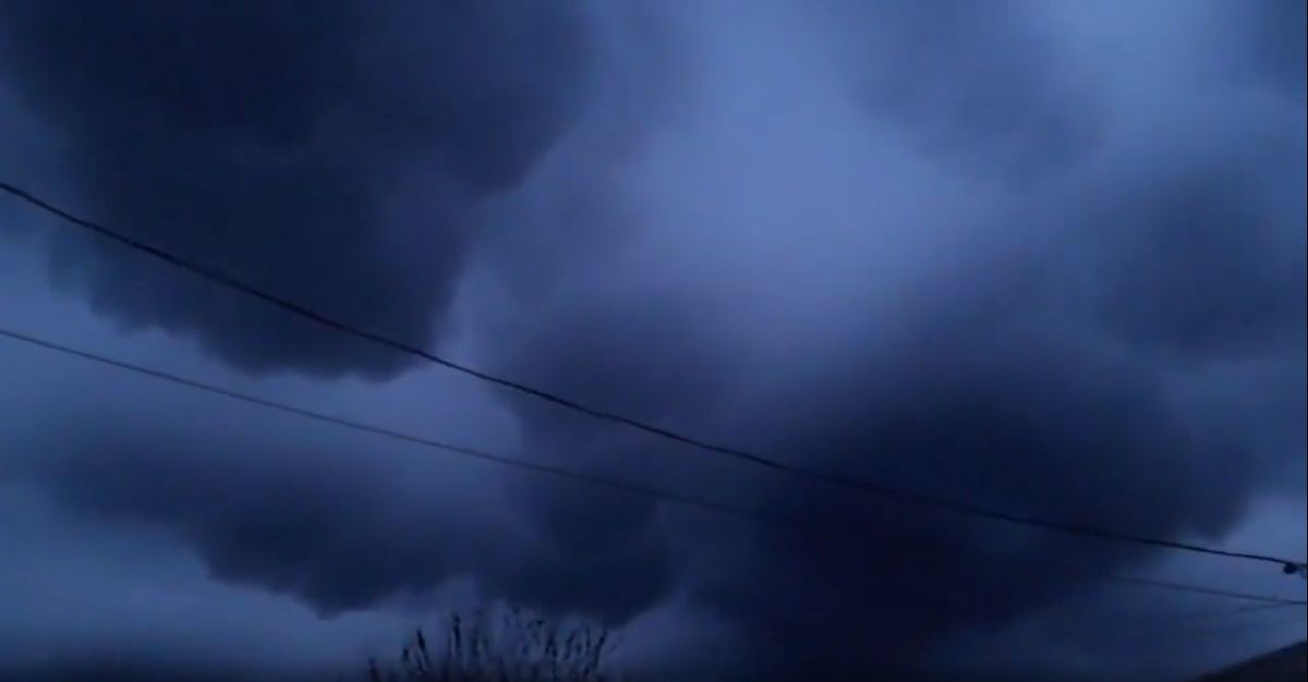 Dark black and blue clouds fill the frame. A power line runs through them. You can slightly see a tree on the bottom of the photo, as well as a house to the right. 