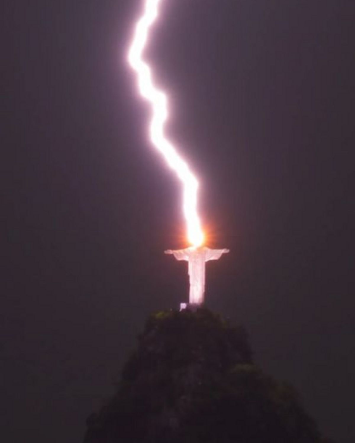 A thick bolt of lightning hits a large statue that's located on a cliff.