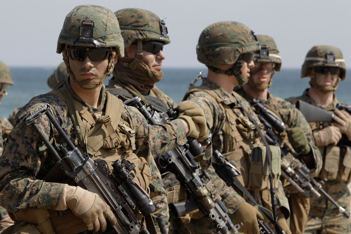 Several people in camouflage holding guns stand near an ocean.