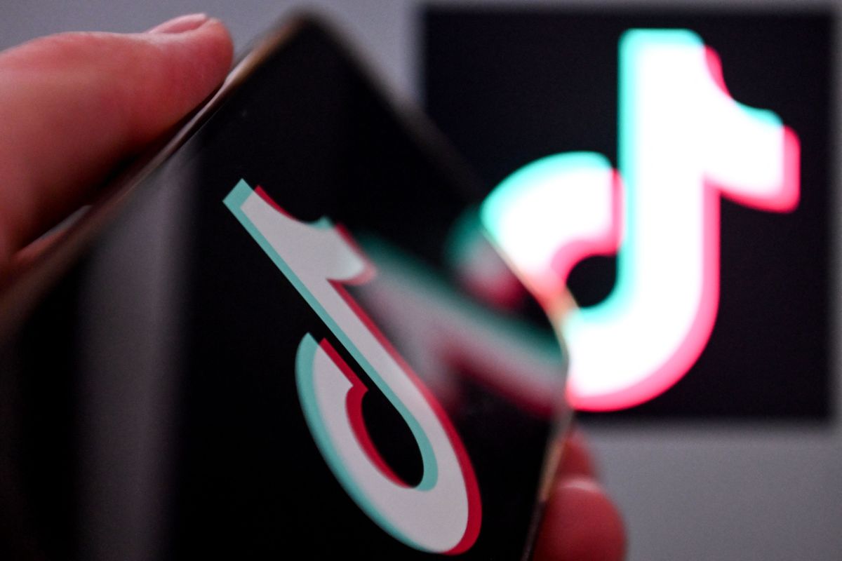 TikTok's logo is on both a phone and in the background of a bigger screen.