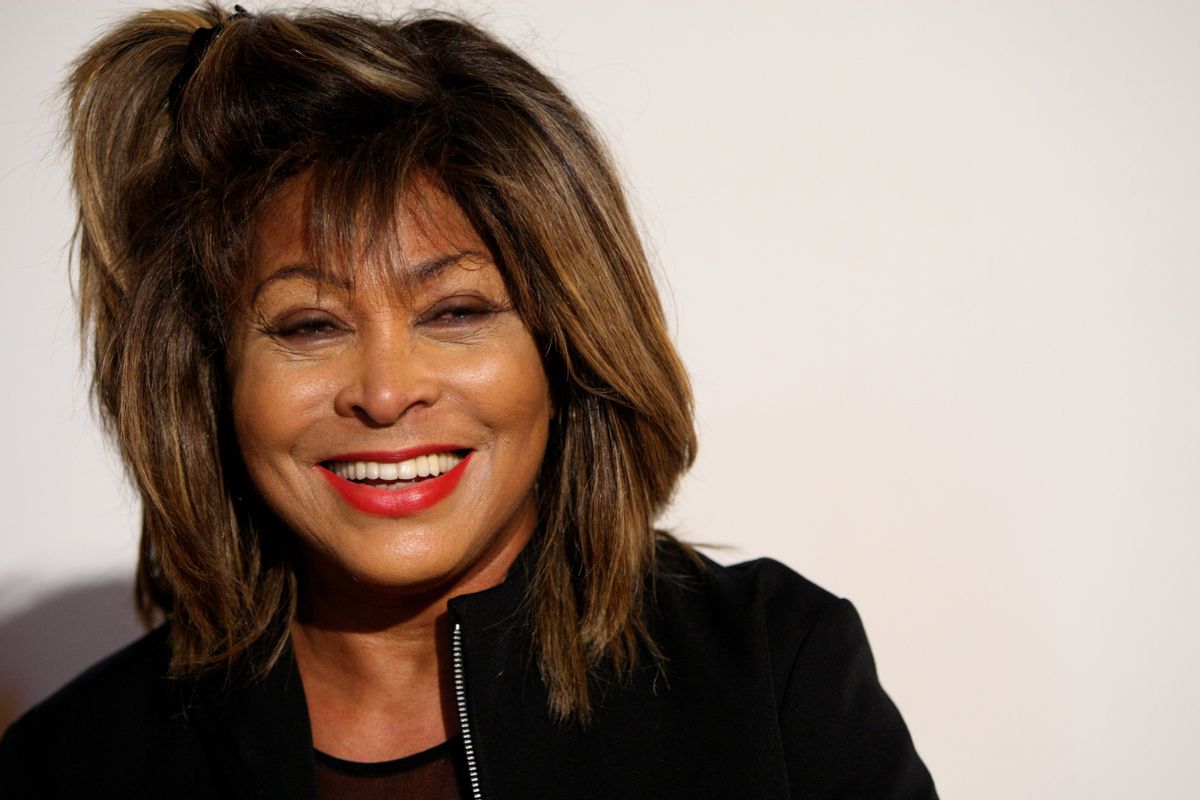 A Black woman wearing a black jacket and red lipstick smiles.