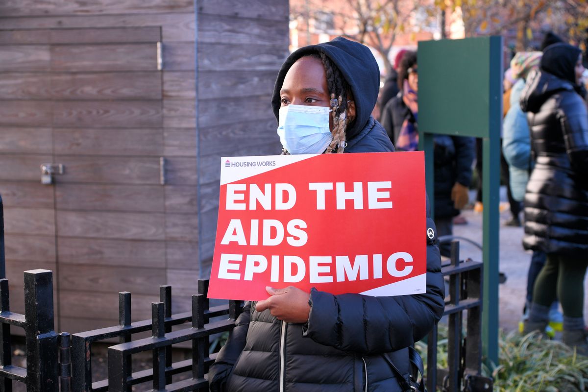 A Black person holds a red sign with white letters that say "END THE AIDS EPIDEMIC."
