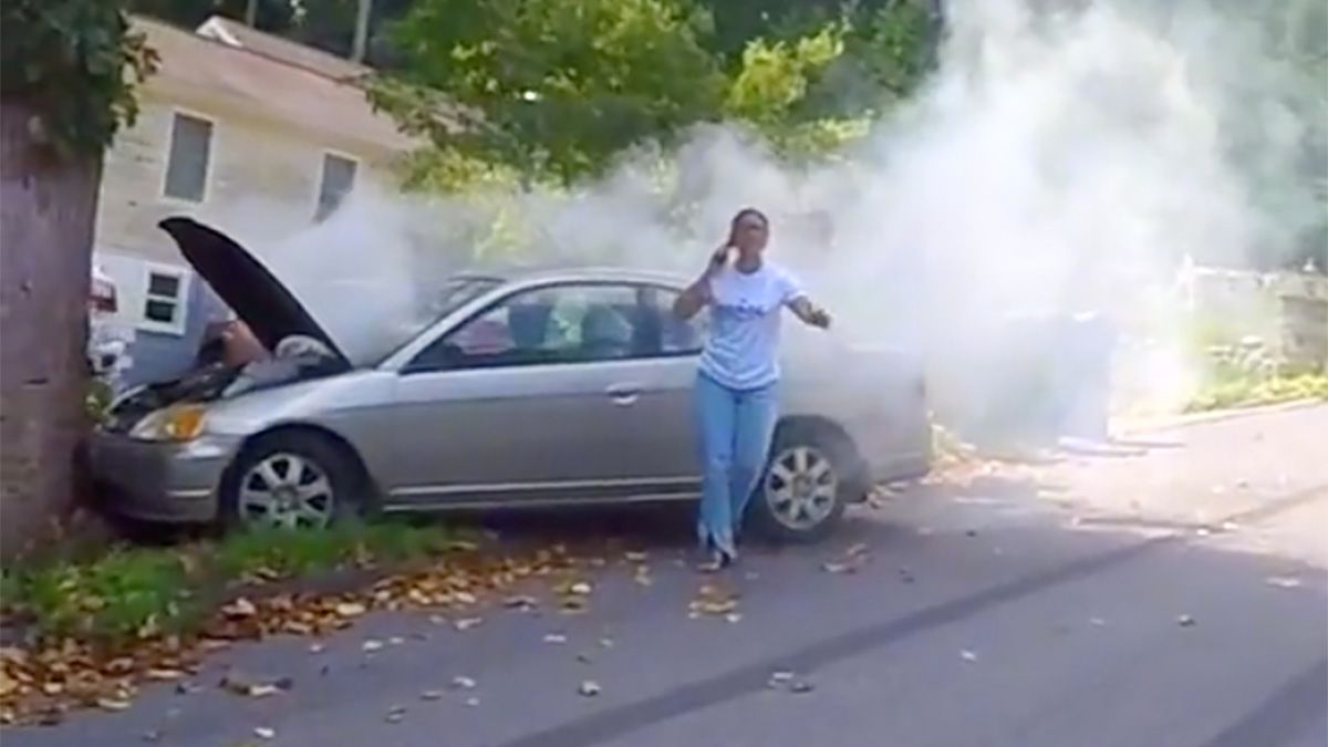 A video showed a woman who appeared to have crashed her car into a tree telling a man careful it's gonna blow and he responded by telling her you can't park your car here ma'am.