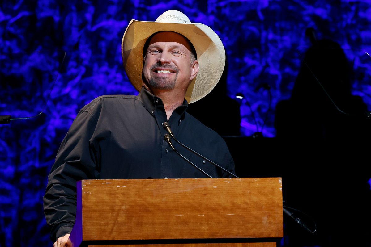A white man wearing a cowboy hat stands before a podium smiling.