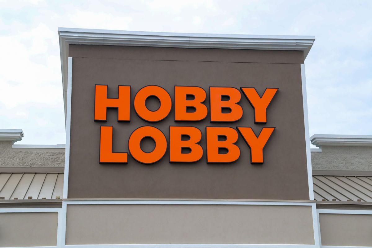 A brown building with the words "Hobby Lobby" in orange is pictured. In the background is a light blue sky with white clouds.