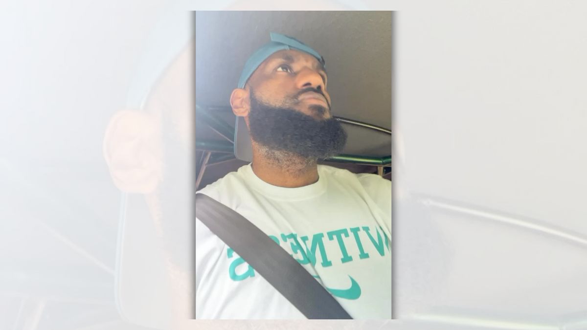 A Black man wearing a backwards blue hat is in a vehicle looking up towards the road.