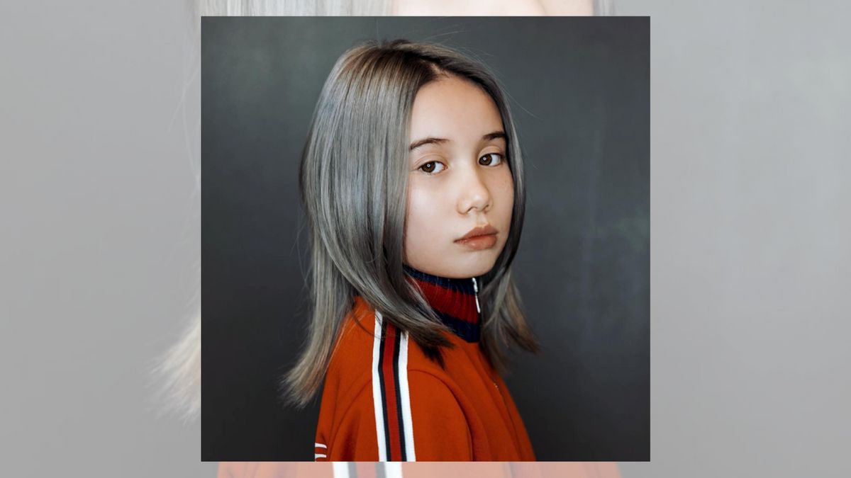 A white girl with silver hair in an orange jacket looks towards the camera.