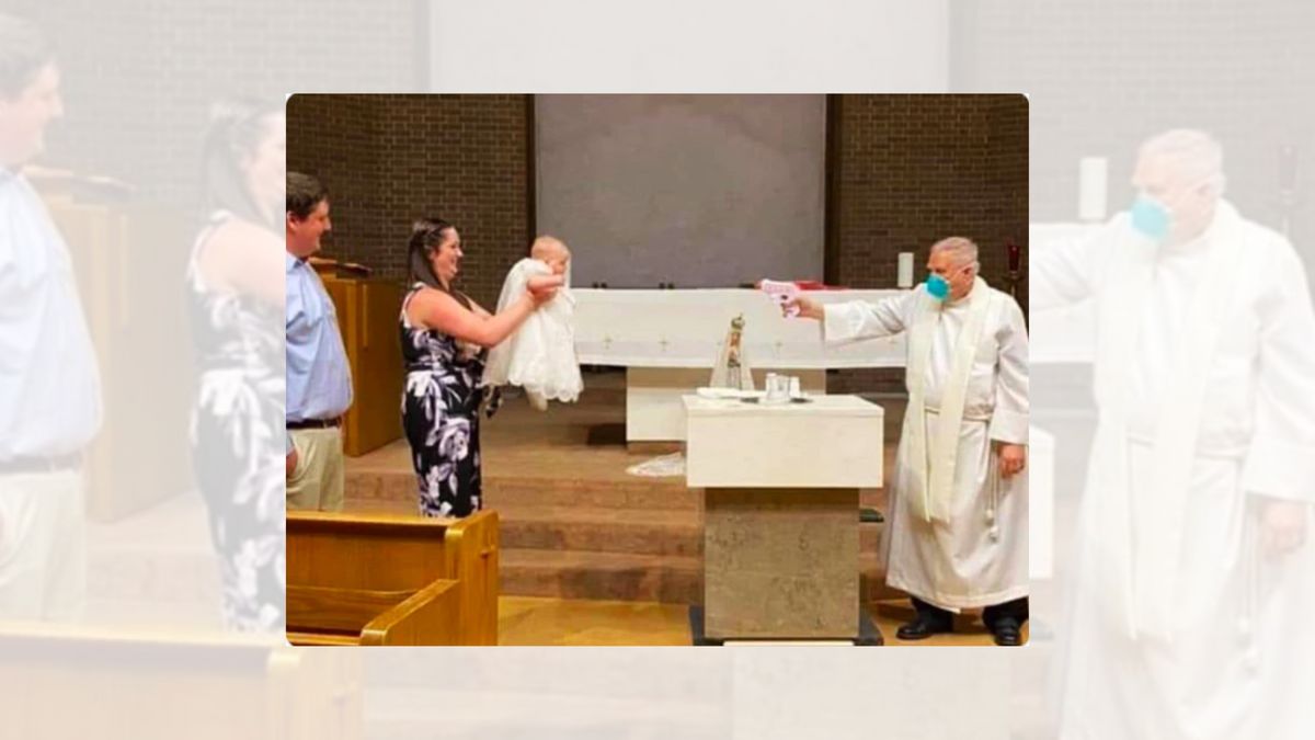 A priest wearing a mask points a water gun at a baby and their family.