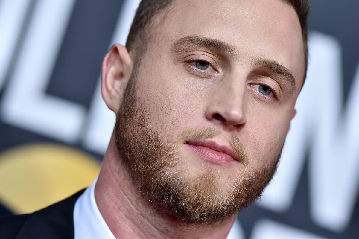 A white man wearing a suit looks towards the camera.