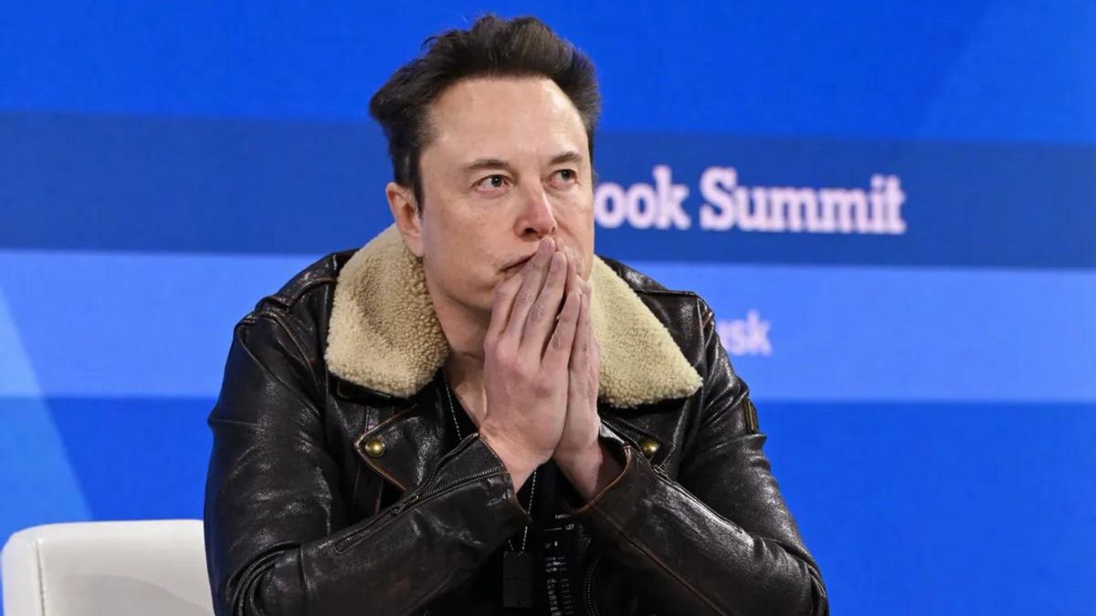 A white man wearing a black jet has his hands held to his mouth.