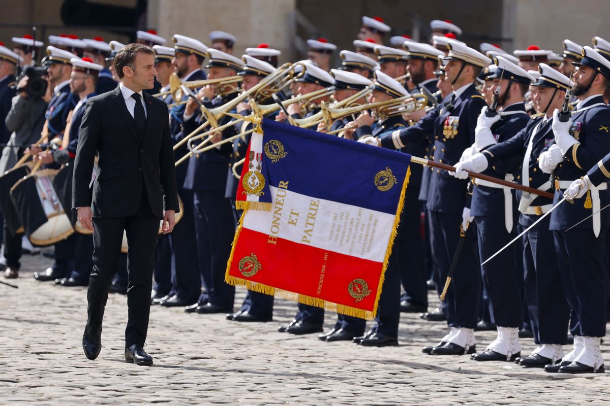 A white man wearing a black suit walks in front of a crowd of soldiers. Several are holding instruments like trombones and drums.