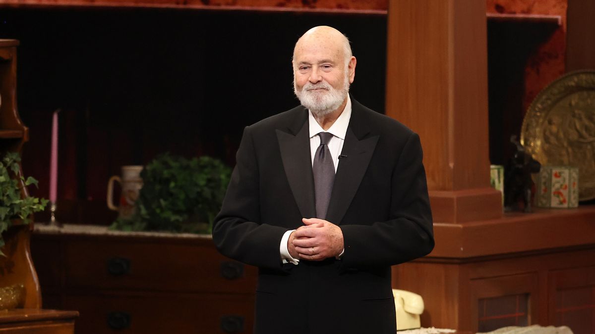 A white man wearing a black suit holds his hands clasped.