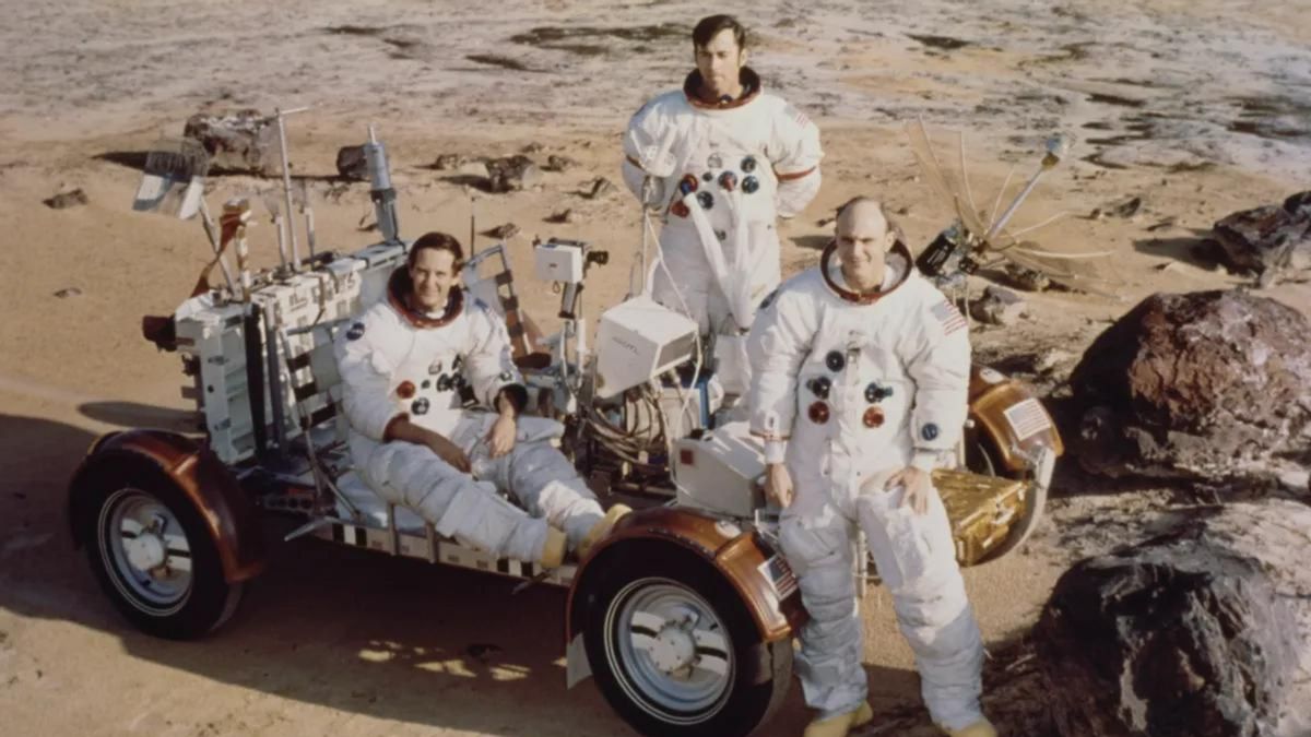  Three white man wearing astronaut suits stand around a buggy.