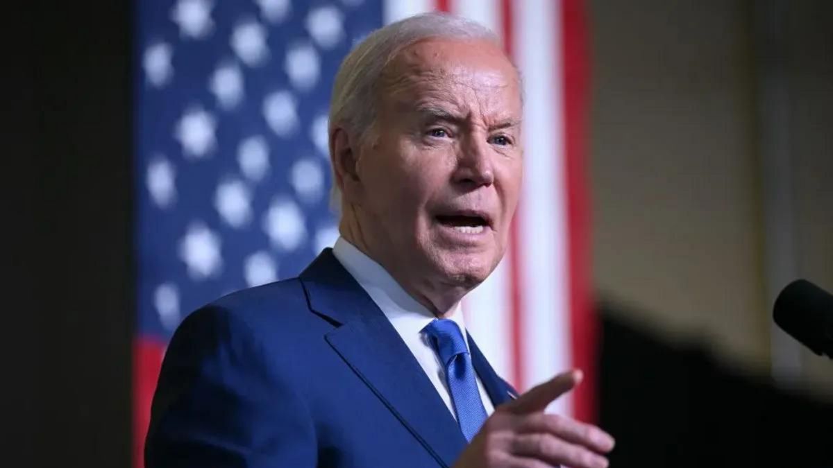 A white man wearing a blue suit points his index finger as he speaks.