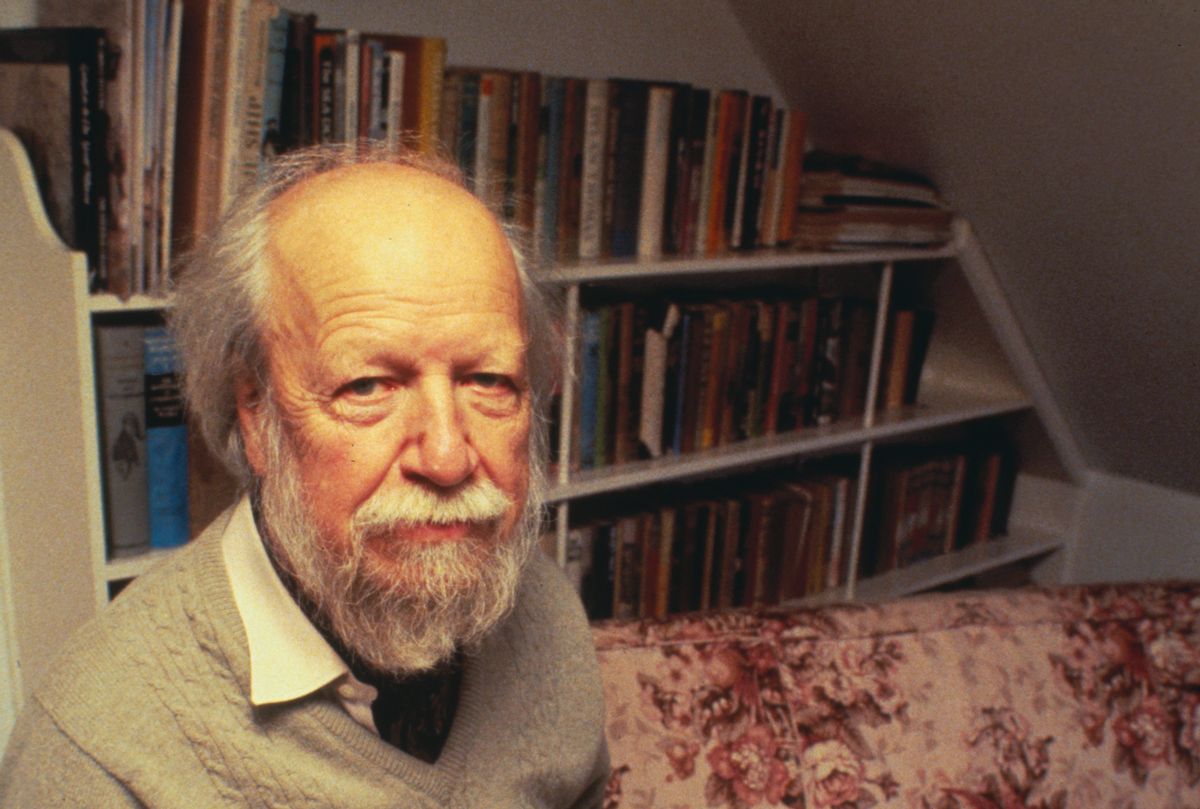 A white man is pictured in front of shelves full of books.