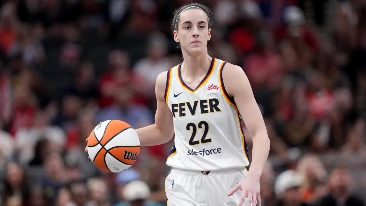 A white woman wearing a uniform that says FEVER holds a basketball in her left hand.