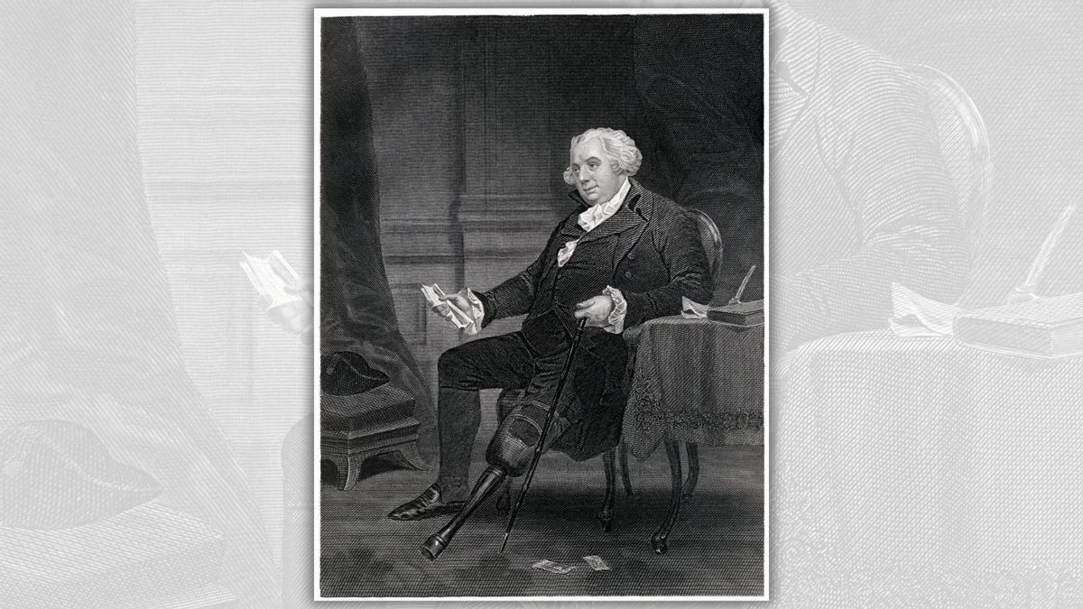 A white man sits in a chair holding a document in his left hand.