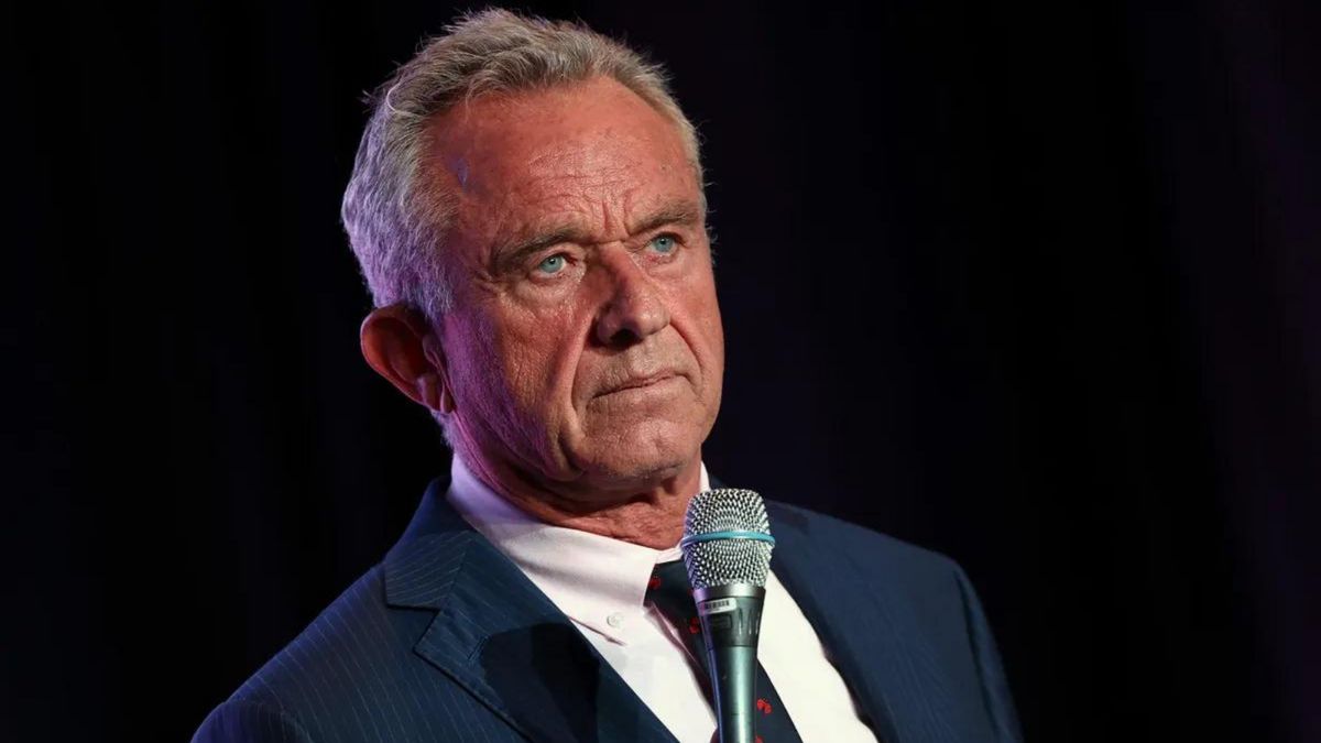A white man wearing a blue suit holds a microphone near his mouth.