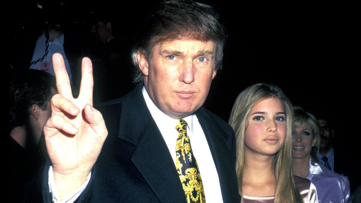 A white man wearing a black suit puts up a peace sign next to a white girl. Both are looking at the camera.