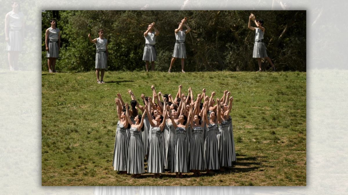 A group of women are centered in the grass. Above them, five men are standing, some with their arms stretched above their heads.