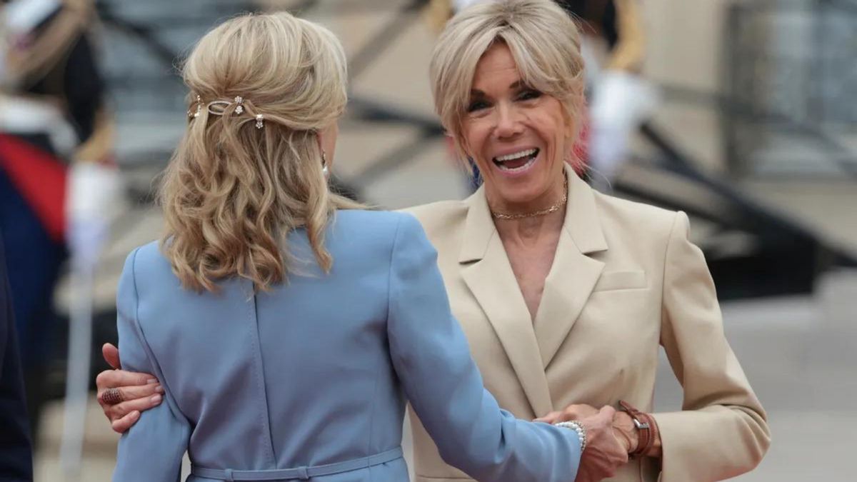A white woman smiles while shaking another white woman's hand.