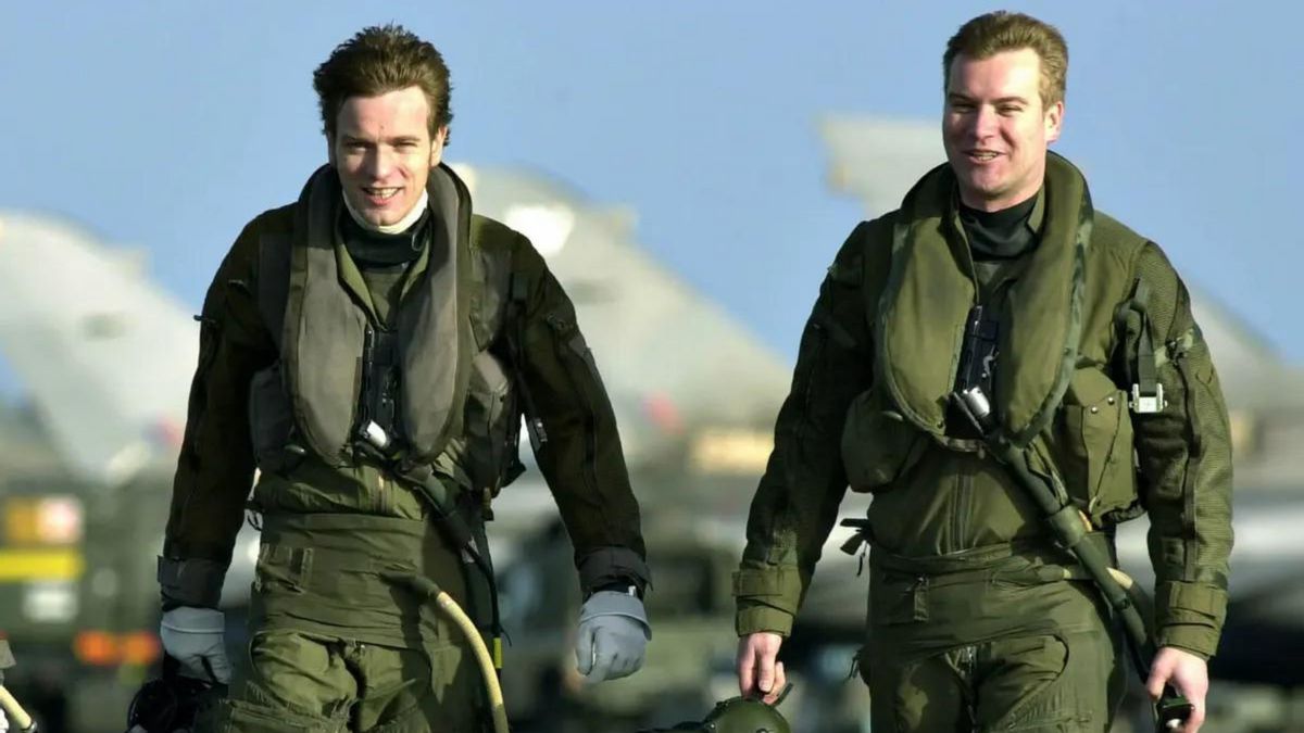 Two white men walk next to each other wearing green uniforms.