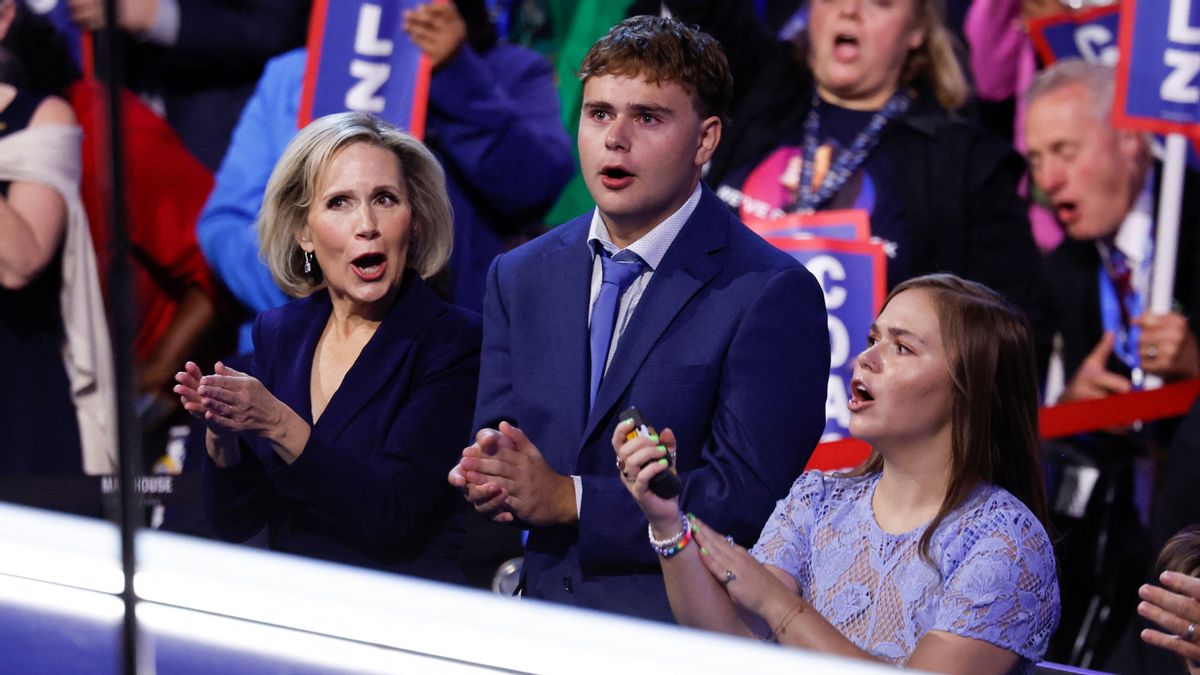Two white women surrounding a white boy clap. The boy is wearing a suit, while the women are wearing dresses, all of which are blue.