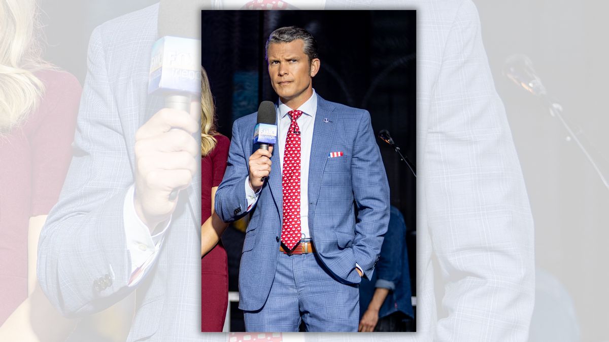 A white man wearing a blue suit holds a microphone in his left hand.