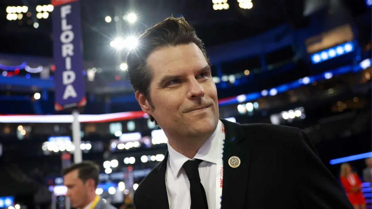 A white man wearing a black suit looks pleased. In the background, you can see a sign that says FLORIDA.