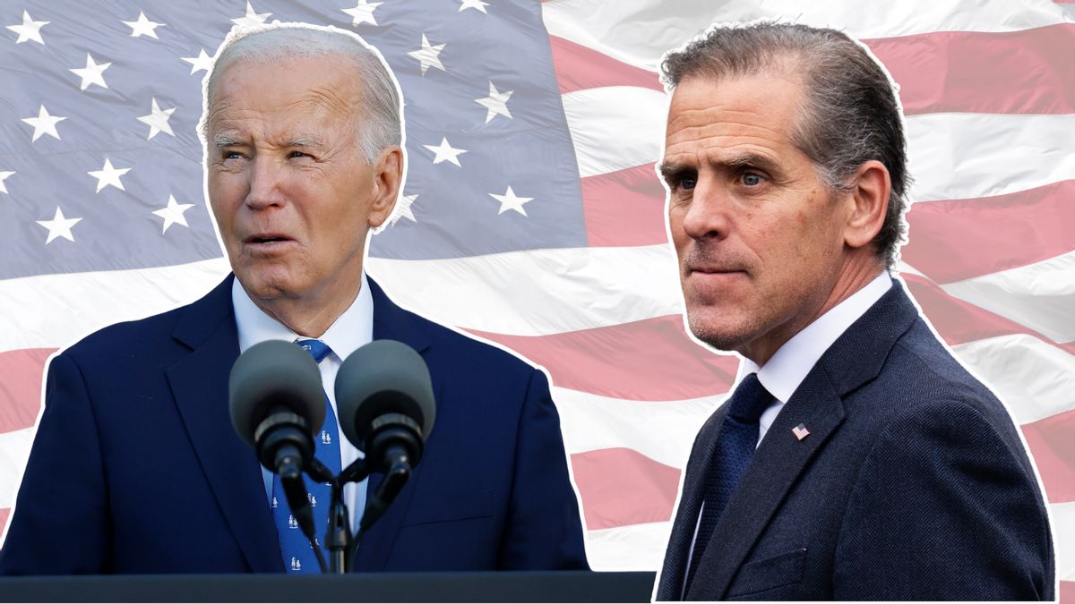 A white man wearing a blue suit standing at a microphone stands next to another white man wearing a gray suit. In the background is a red, white and blue flag.
