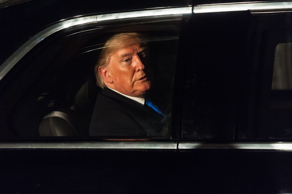 U.S. President-elect Donald Trump, a man with an orange tan and blonde hair, in a suit with his face partially obscured in shadow sitting in a black car. 