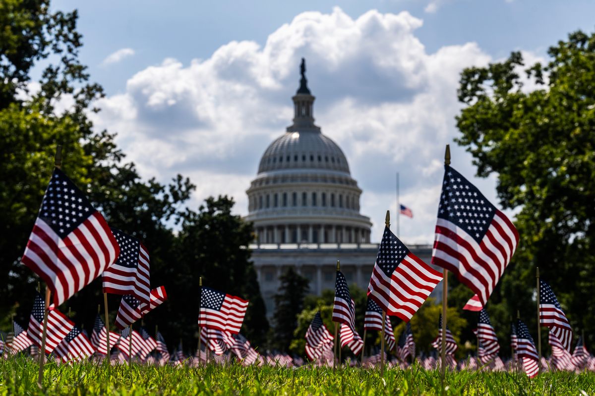 The U.S. Capitol dome, a white building that is dome-shaped, in the backdrop, with many small U.S. flags upright in the grass. 
