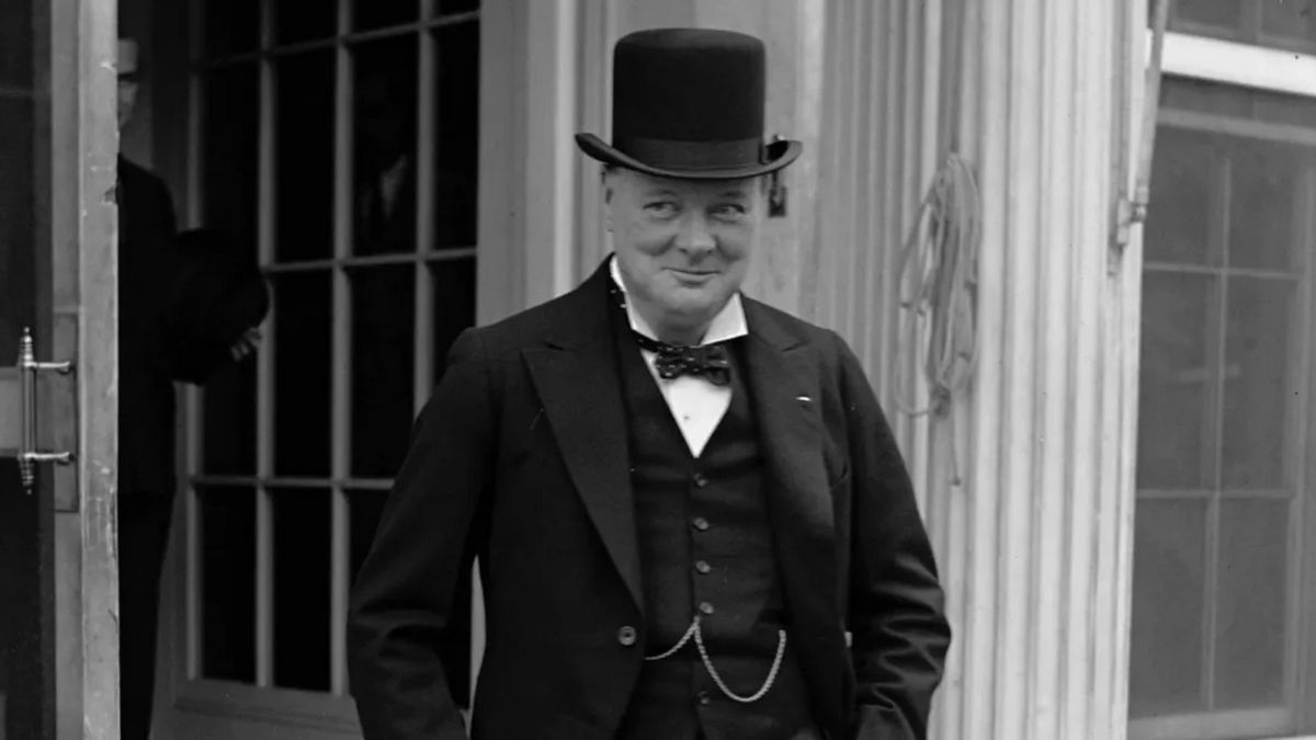 A white man wearing a black suit is shown smiling.