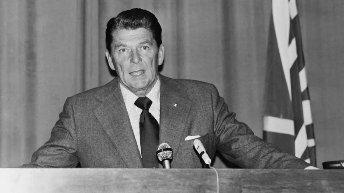 A white man sits at a desk in a black and white photo.