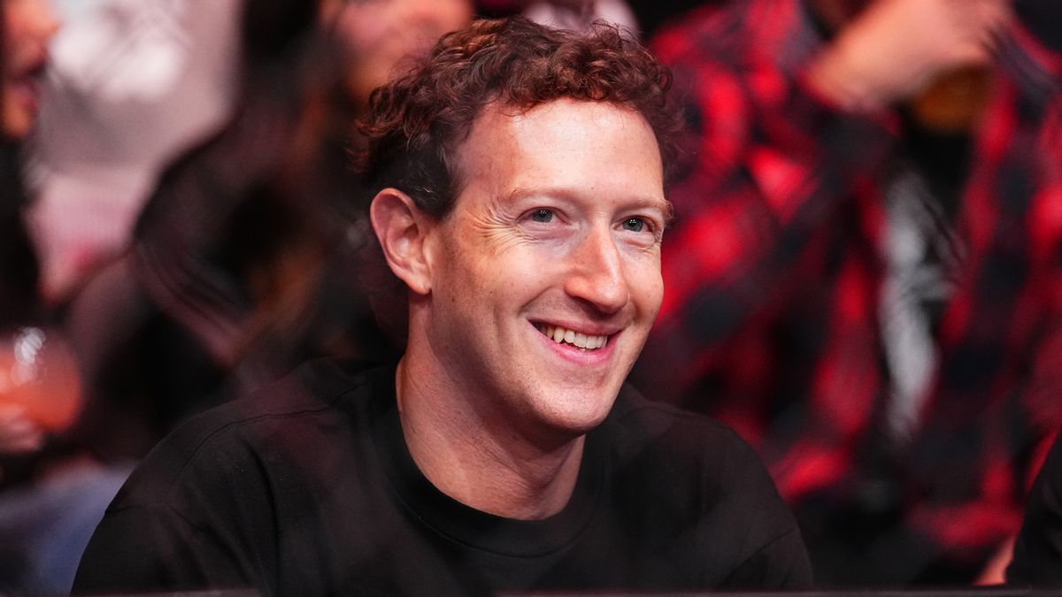 A white man smiles while looking forward. People can be faintly seen sitting behind him.