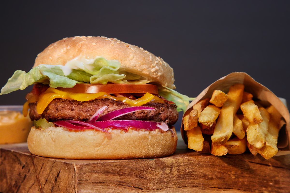 A burger and fries are shown next to each other on what appears to be wood staging.