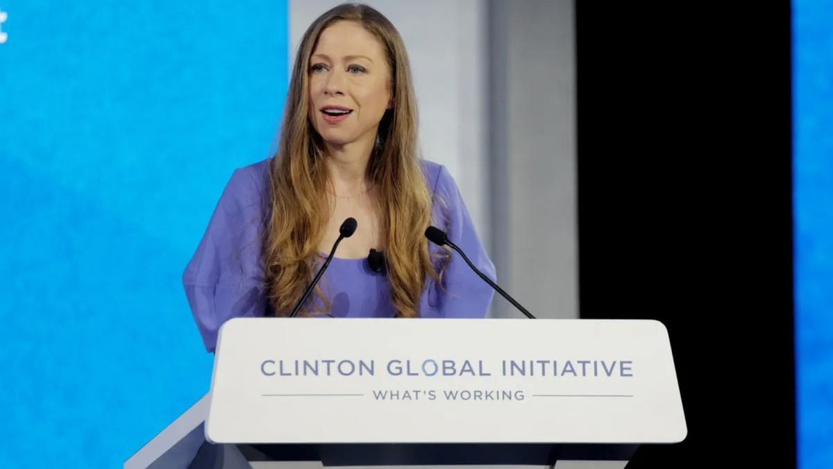 A white woman wearing a purple top looks towards the left. She's standing behind a podium that says CLINTON GLOBAL INITIATIVE in purple. Below, WHAT'S WORKING is also in smaller purple text.