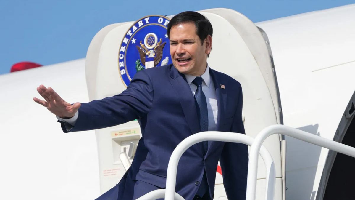 A Latino wearing a blue suit stands on the steps to a white plane. 