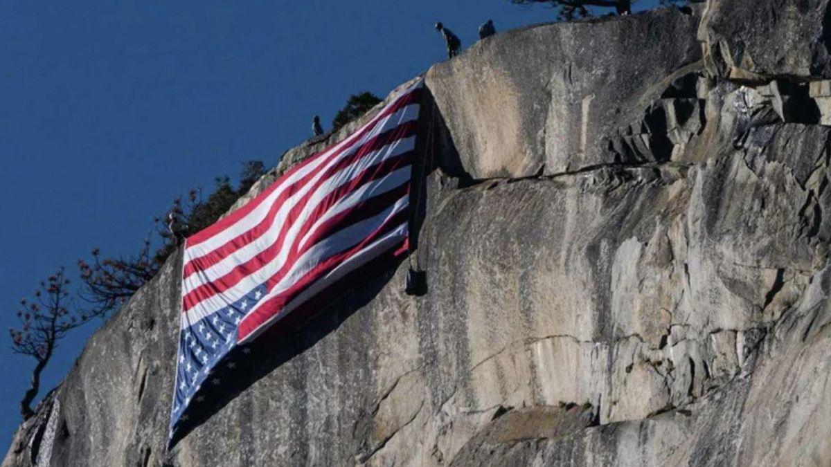 A red, white and blue flag is hung upside down on a large rock formation.