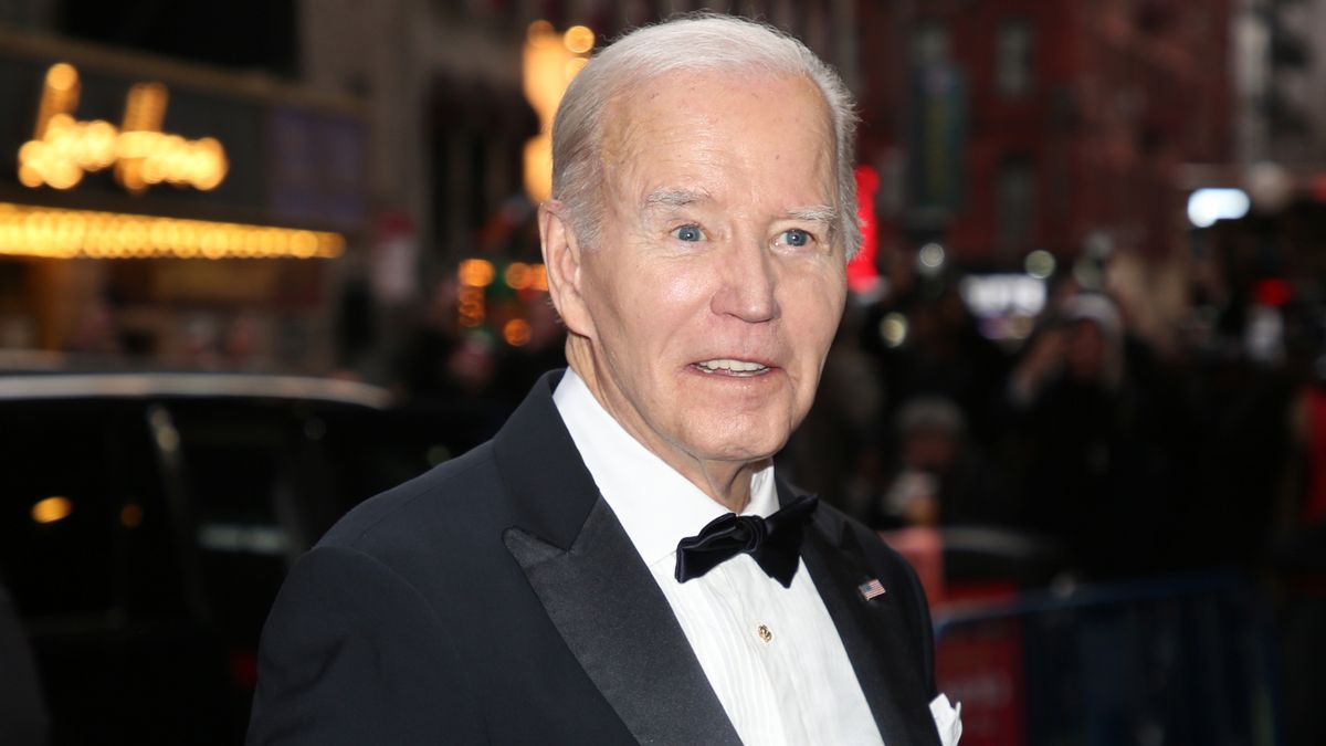 A white man wearing a black and white tuxedo stares towards the camera.
