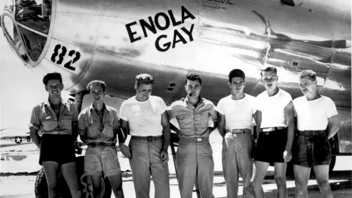 A photo shows a row of people standing in front of a plane that says ENOLA GAY.
