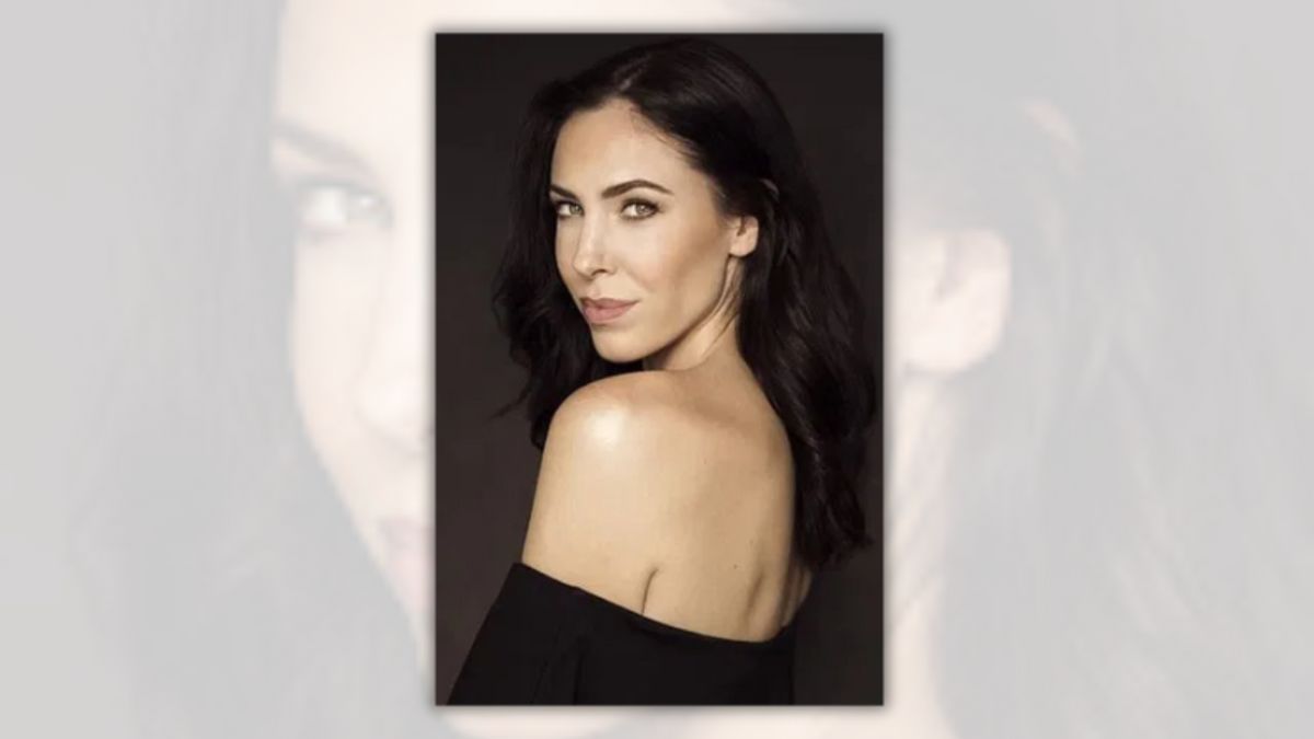 A white woman wearing a black top looks over her left shoulder towards the camera.