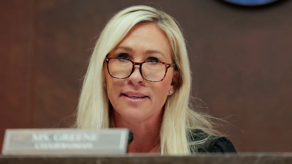 A white woman wearing glasses sits behind a desk.