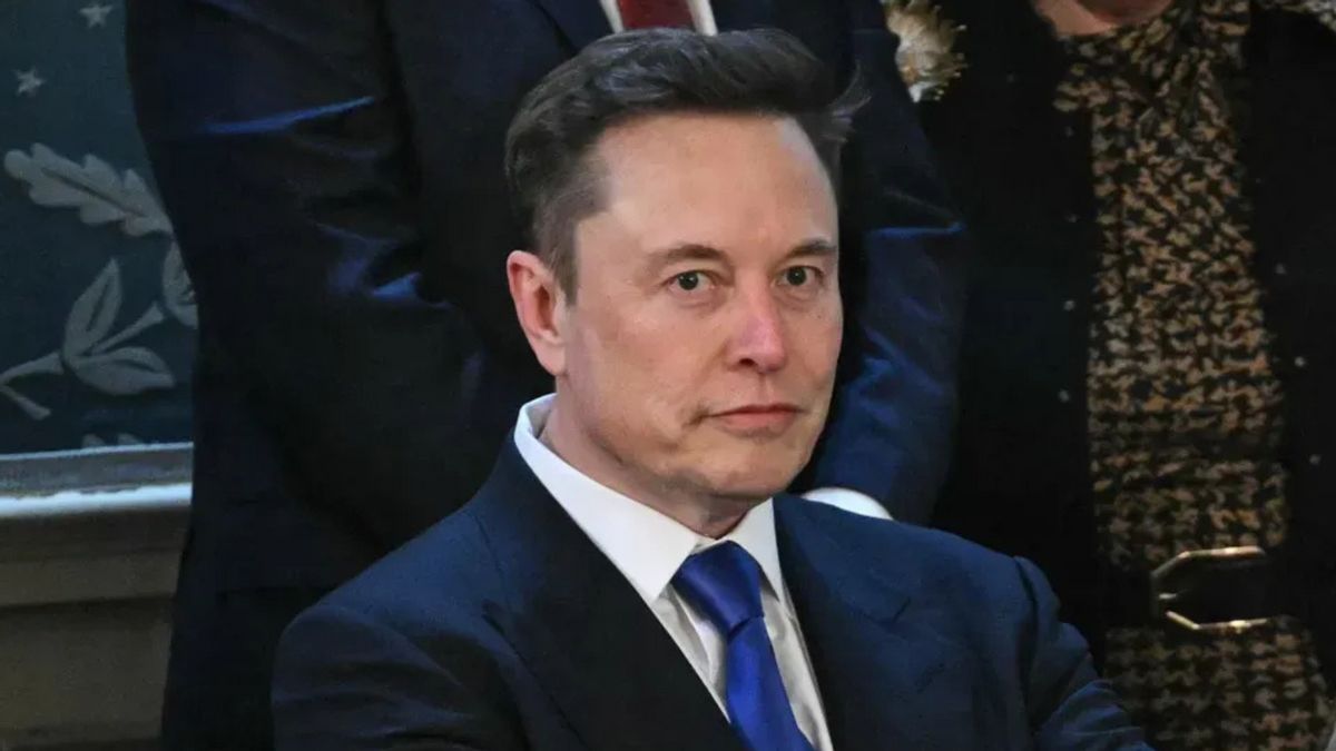 A white man wearing a blue suit looks towards the camera.