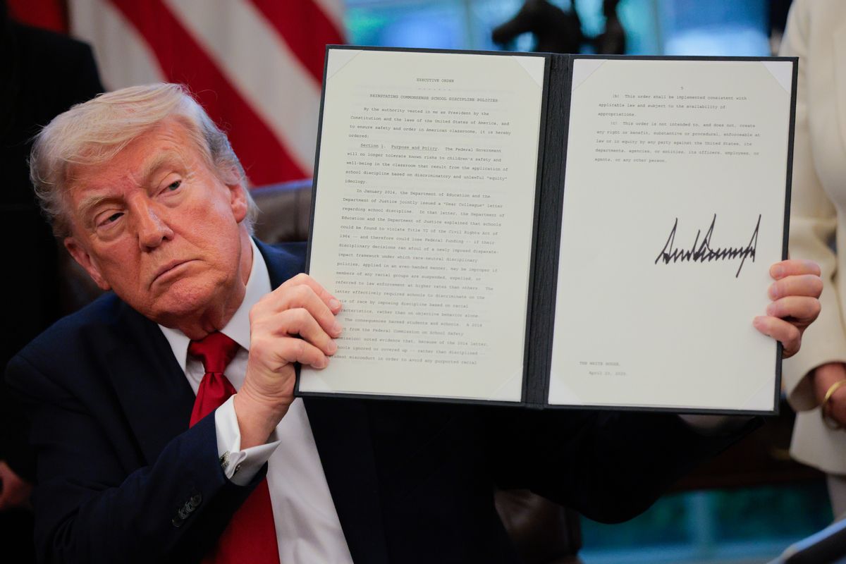 A white man in his late 70s wearing a suit holds up a signed document. 