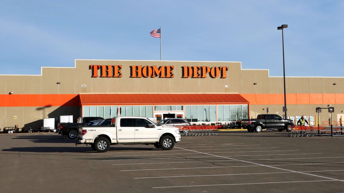 A store that says THE HOME DEPOT in orange letters is shown, with its parking lot in front of it. An American flag is on top of the store.