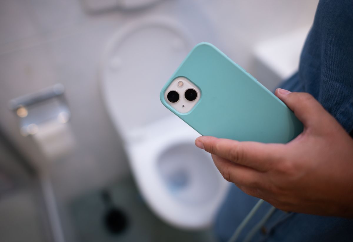A phone with a light blue phone case is helf by a person. In the background, you can see a toilet.